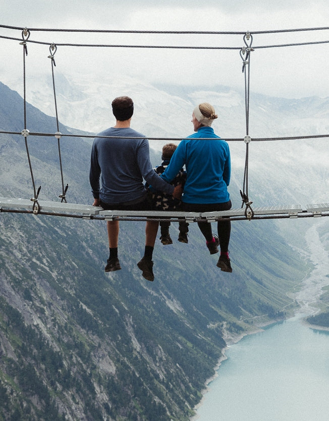 A family sits on a bridge over a mountain gorge