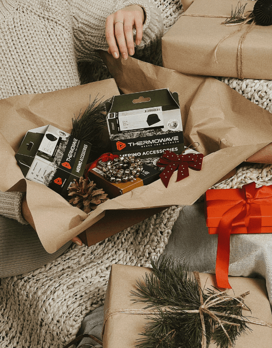 woman holding a full gift box with thermowave clothing and Christmas decorations